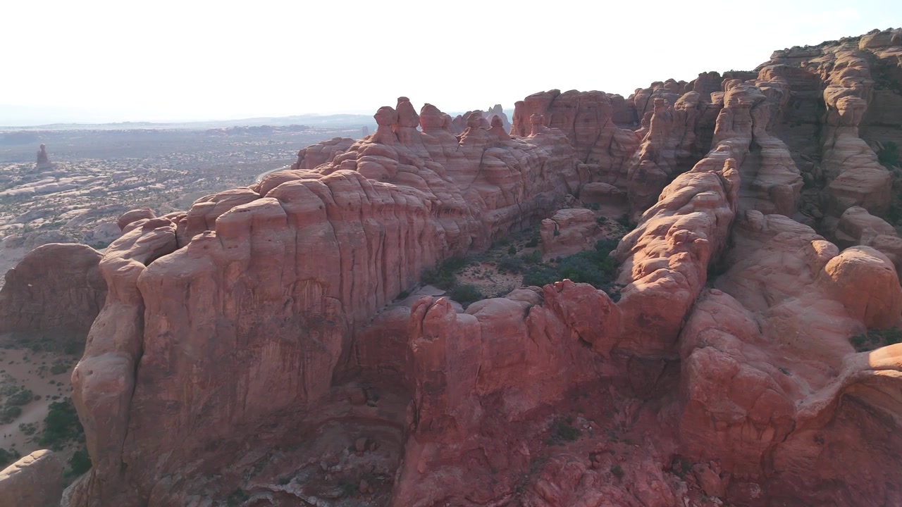 Splendido filmato stock del Parco Nazionale di Arches, USA, durante un pomeriggio luminoso. La luce solare brillante illumina le maestose strutture di arenaria rossa e il paesaggio desertico sotto un cielo azzurro limpido.