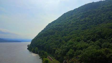 aerial drone footage of freight train tracks along the hudson river in new york's hudson valley during early autumn with mountains and a river and forests