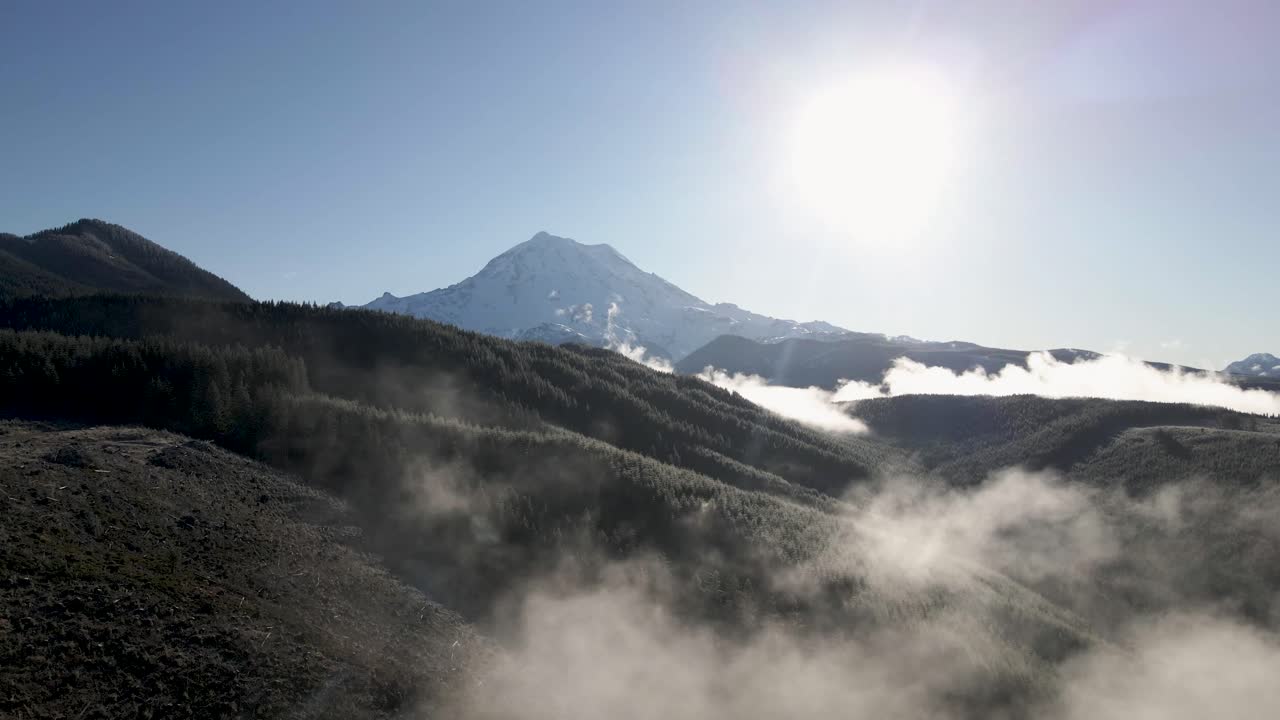 niebla esparcida a lo largo de un valle boscoso, revelando el monte rainier y el sol, aéreo