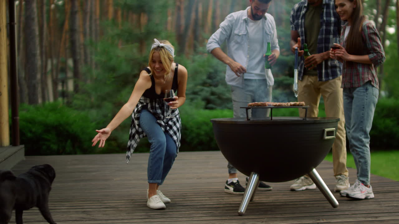 chicos relajándose cerca de la barbacoa afuera. mujer sonriente llamando a perro en el patio trasero.