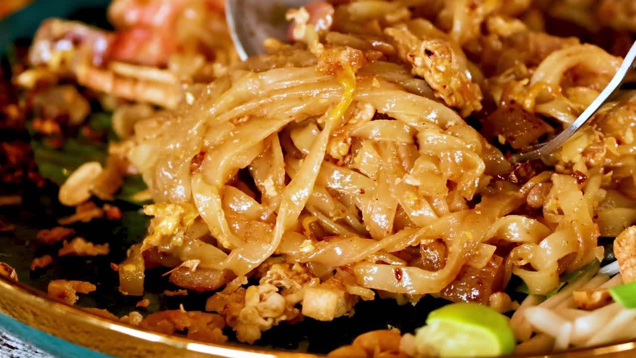 A detailed view of noodles being stirred with shrimp and garnishes on a plate.