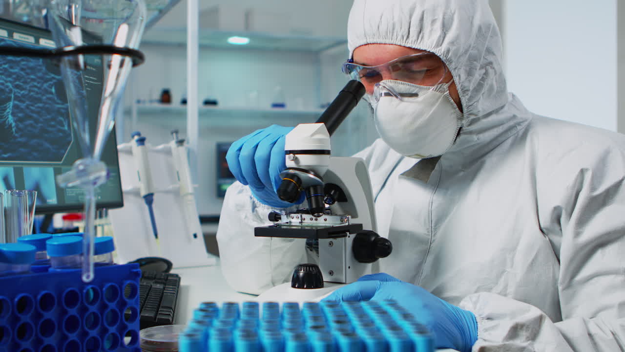 Biological scientist in coverall using microscope doing research