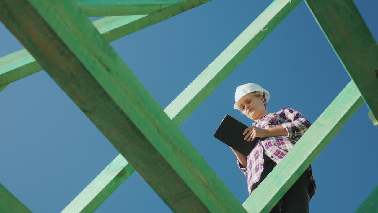 una arquitecta está trabajando con una tableta entre las vigas de la supervisión arquitectónica del techo