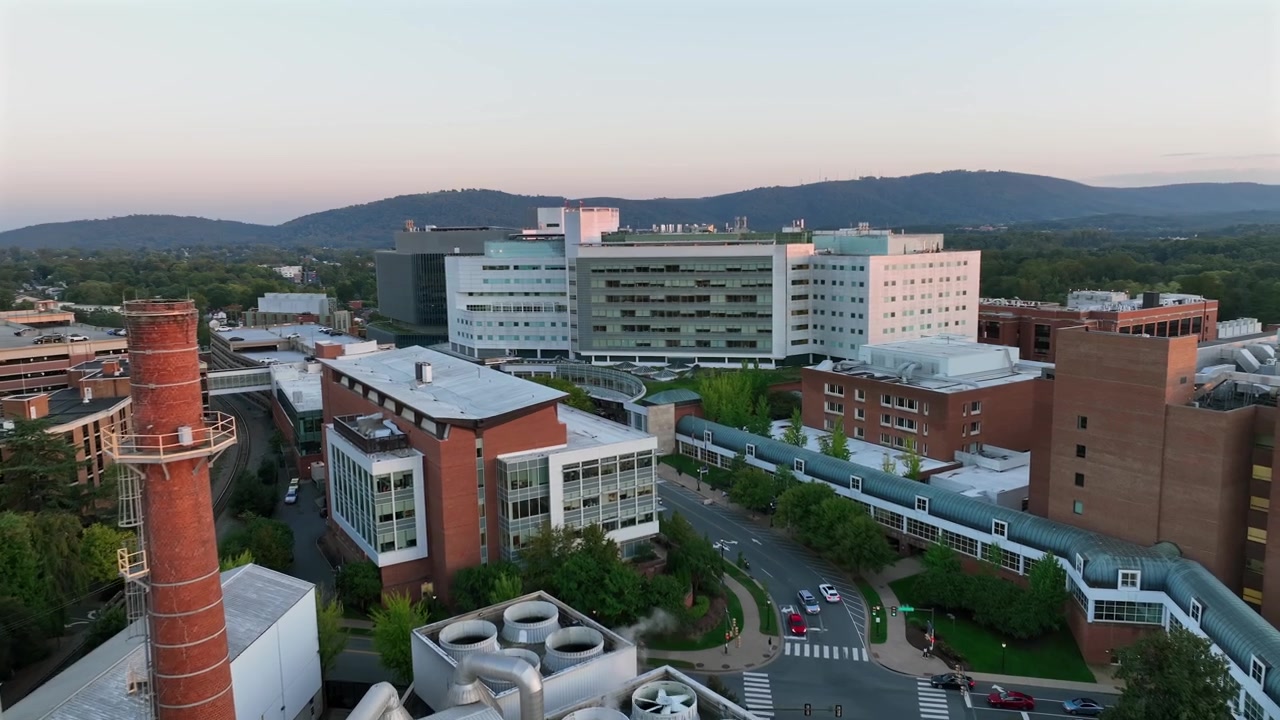 Sorvolo aereo di una fabbrica industriale con ciminiera e dell'Università della Virginia durante un'alba dorata. Inquadratura in avvicinamento. Strada con auto al mattino.