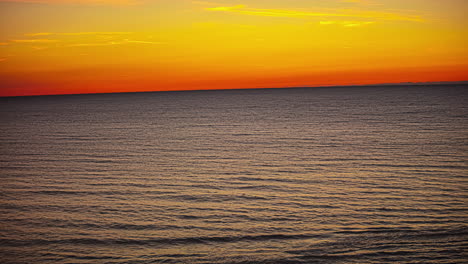 time lapse shot of golden hour with orange sky at horizon behind ocean