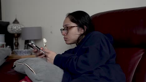 a person enjoys ice cream while lounging on a sofa in a cozy home environment, casually glancing at the display of a mobile phone screen