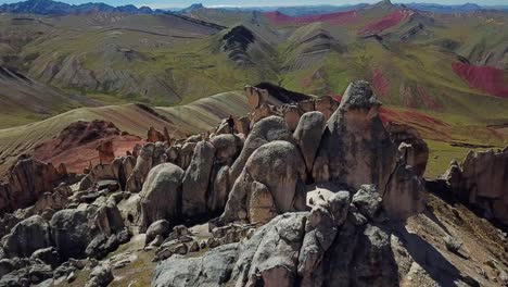 aéreo, marcha atrás, drone disparó lejos de un hombre parado sobre enormes rocas, en la montaña del arco iris de palccoyo, en el valle rojo, andes, perú, sudamérica