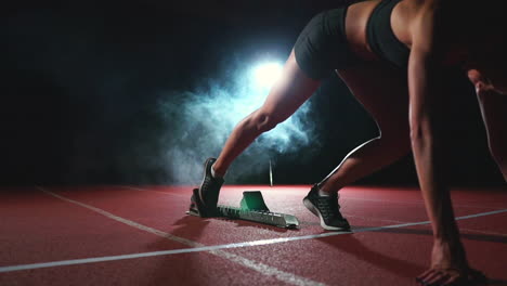 Young-woman-athlete-in-black-shorts-and-a-t-shirt-is-preparing-to-start-in-the-race-for-100-meters-on-the-treadmill-near-the-start-line