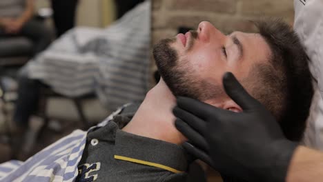 Client-with-black-beard-during-beard-shaving-in-barber-shop.-Groom,-masculine