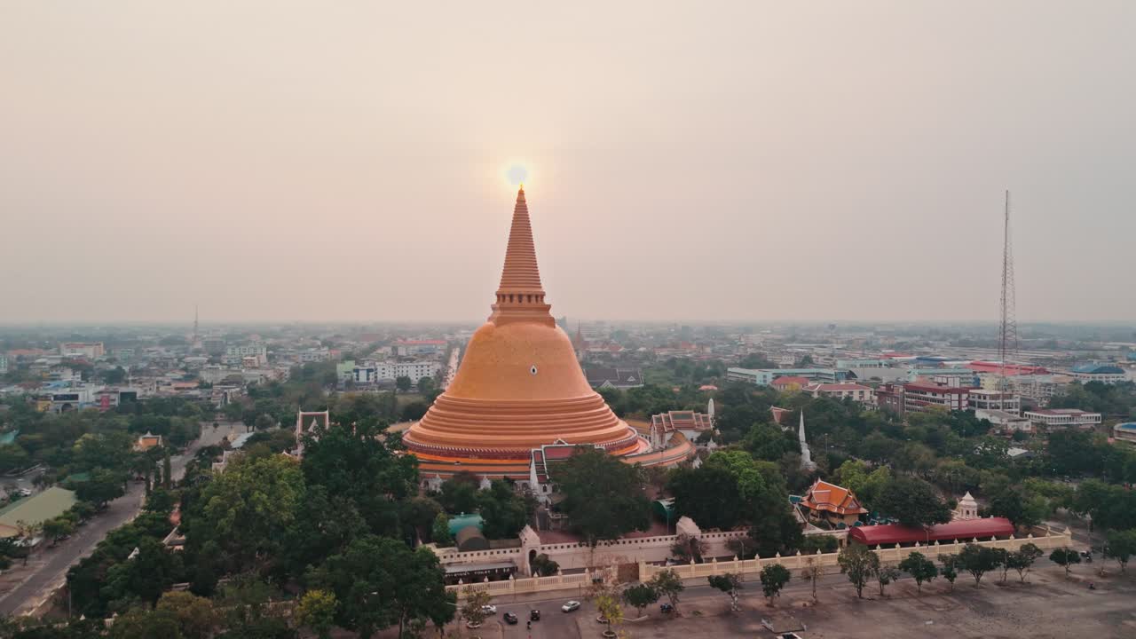 Góc nhìn drone từ trên cao ghi lại bảo tháp vàng khổng lồ vươn lên trên trung tâm đô thị. Mặt trời buổi sáng mờ ảo chiếu thẳng phía sau tượng đài Phật giáo hùng vĩ này thống trị đường chân trời tuyệt đẹp ở Thái Lan
