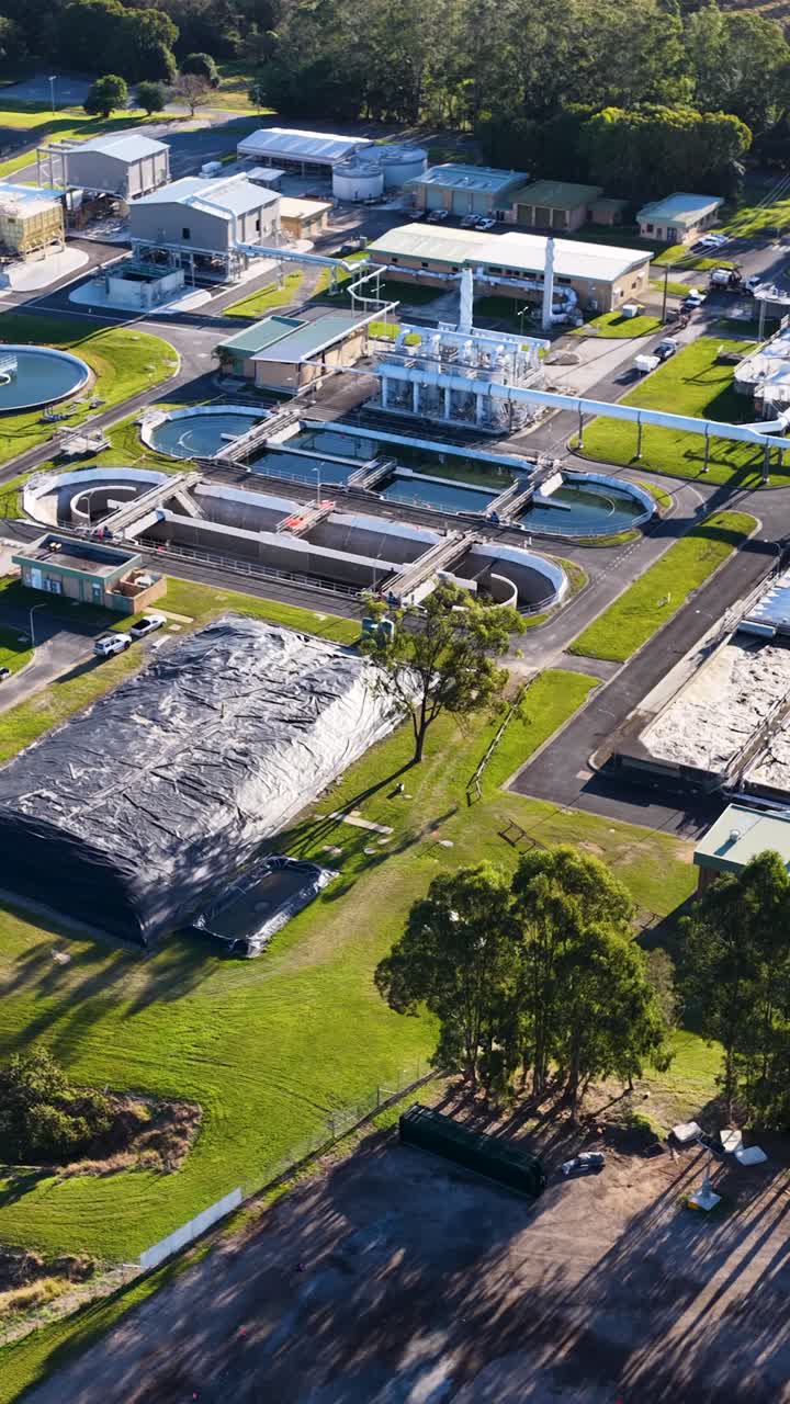 Luftoptagelser panorerer hen over et stort spildevandsrenseanlæg i Gold Coast, Australien, der viser cirkulære tanke, grønne plæner og industriel infrastruktur i skarpt dagslys.