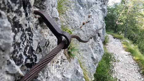 cuerda retorcida de hierro estirada entre rocas cerca del sendero en las montañas