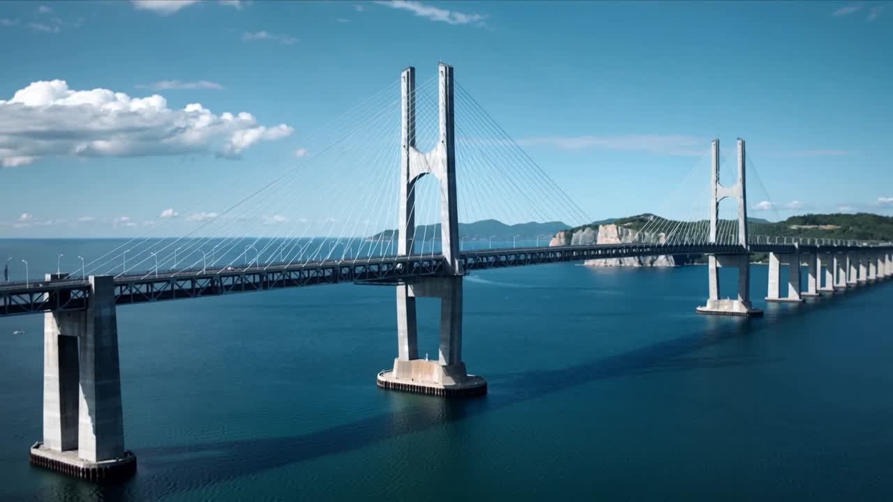 Drone che effettua una panoramica muovendosi a destra e in avanti sopra lo stretto, rivelando un ponte strallato con due piloni.