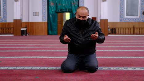 old man wearing mask raising his hands and praying in the mosque