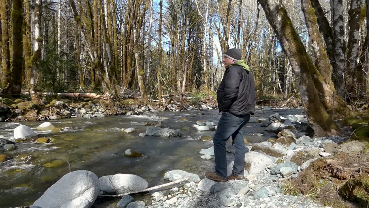 hombre caminando en un bosque mirando el río con grandes rocas en él