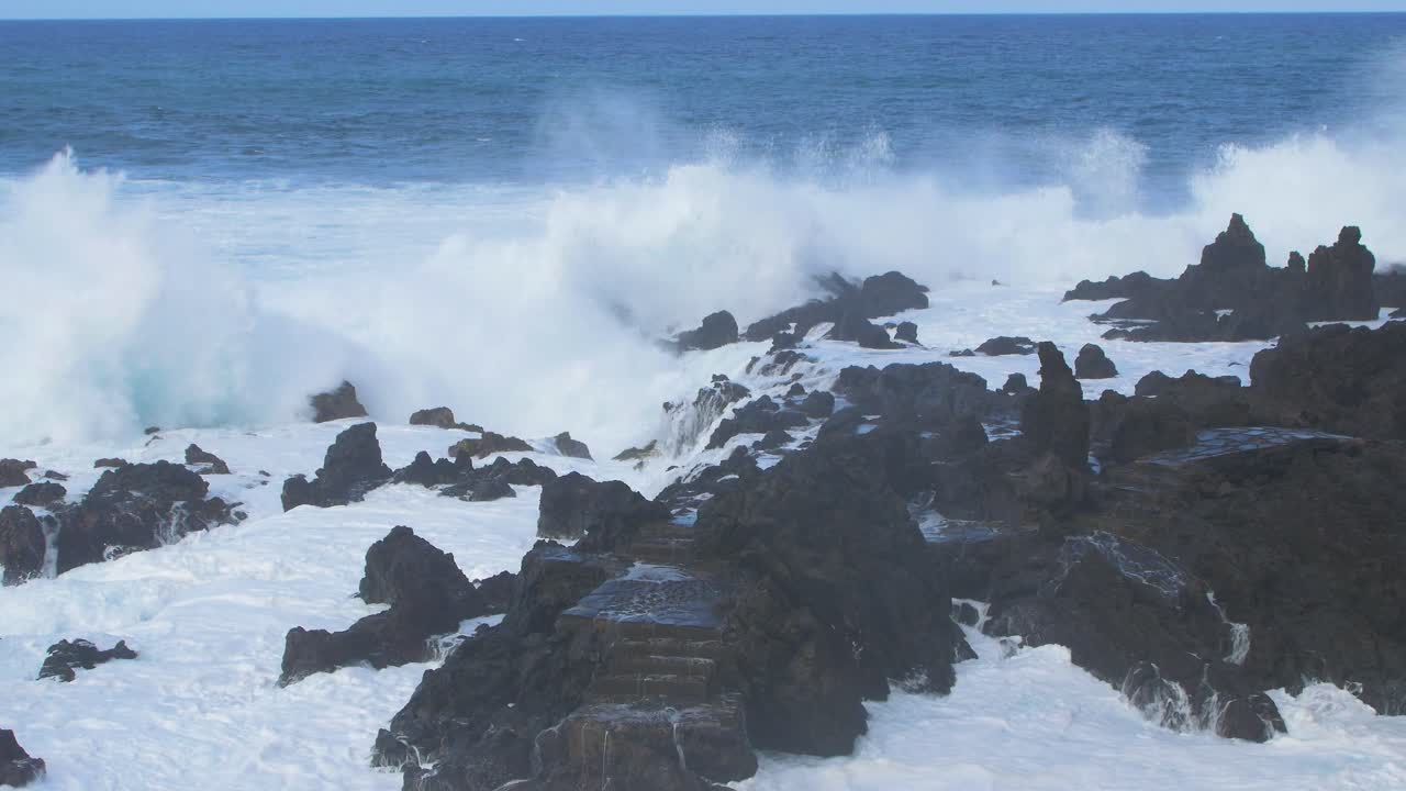 una gran ola del océano atlántico se rompe en una costa rocosa en un día soleado durante una tormenta en puerto de la cruz en las canarias , tiro de mano de gran angular