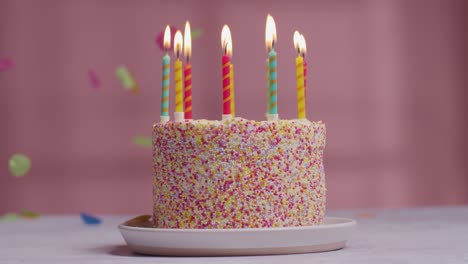 foto de estudio de confeti de papel cayendo sobre pastel de cumpleaños cubierto con decoraciones y velas encendidas 1