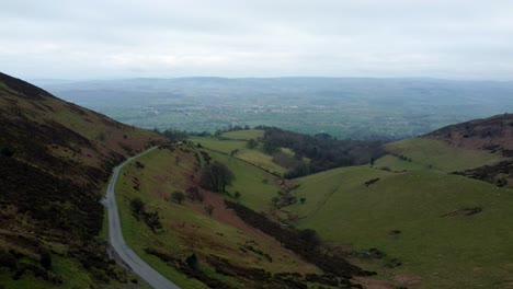 narrow single rural road running through welsh green mountain valleys landscape aerial pull back left