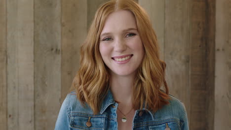 young-stylish-red-head-woman-close-up-portrait-of-beautiful-girl-smiling-happy-at-camera-wearing-denim-jacket-wooden-background