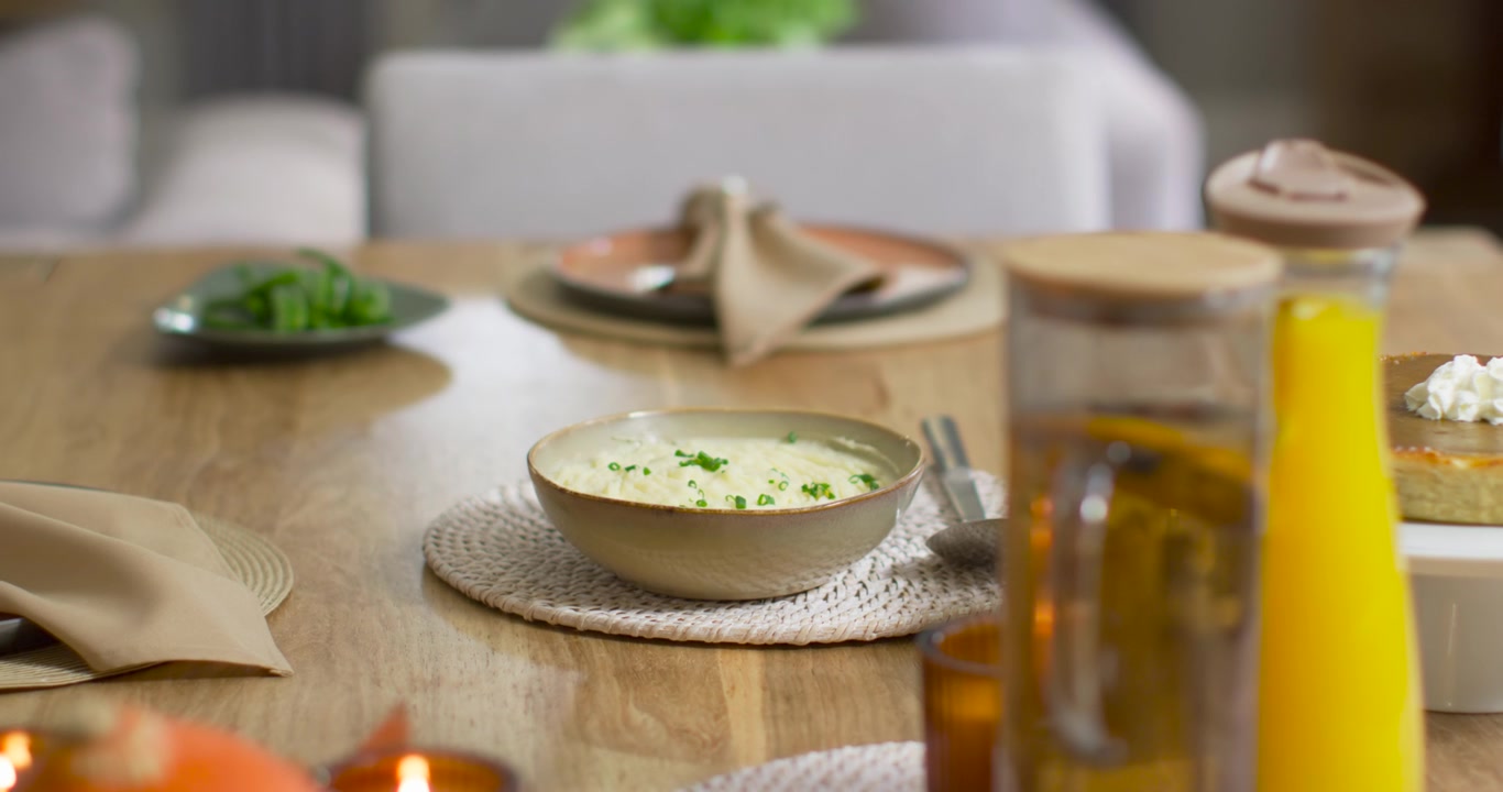 Camera is sliding, showing ceramic bowl of creamy soup; spoon is settling by bowl, preparing meal