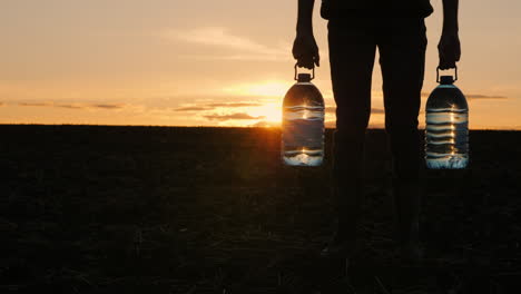 persona que lleva botellas de agua al atardecer en un campo