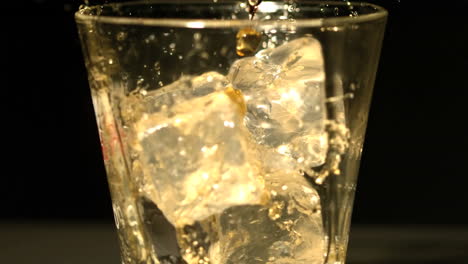 whiskey pouring into tumbler with ice close up