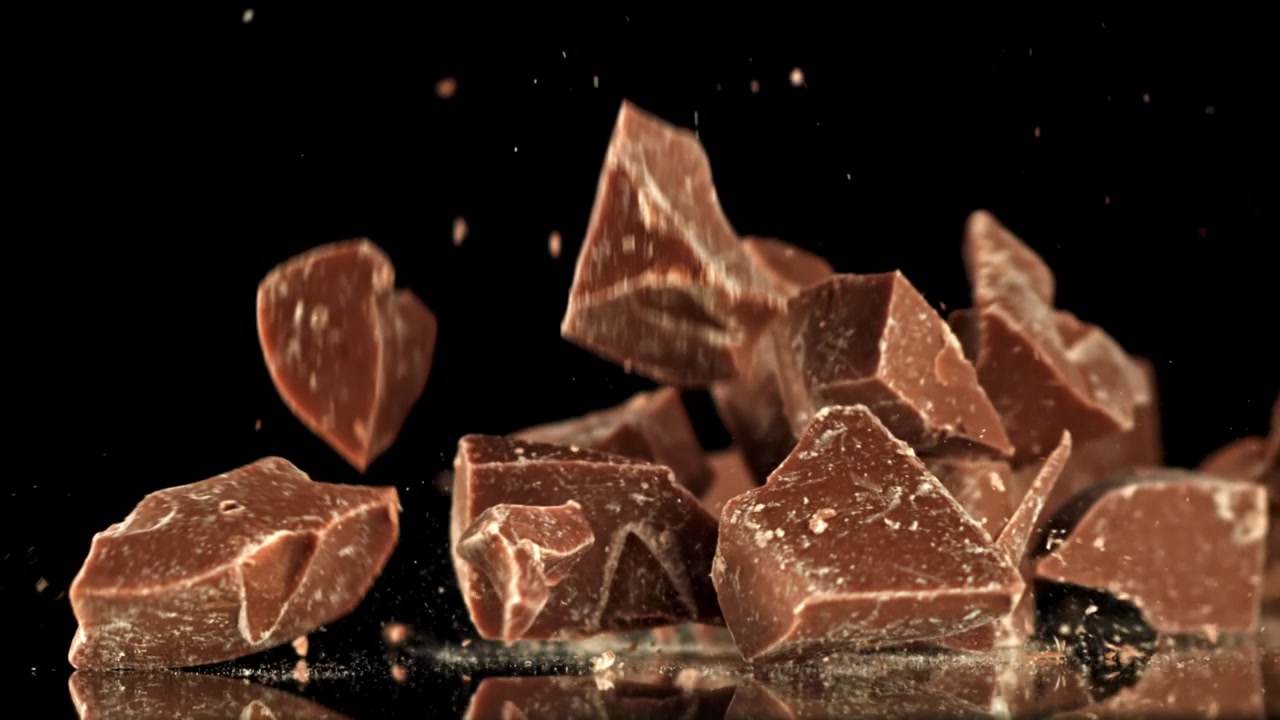 Pezzi di cioccolato che cadono su una superficie nera riflettente al rallentatore