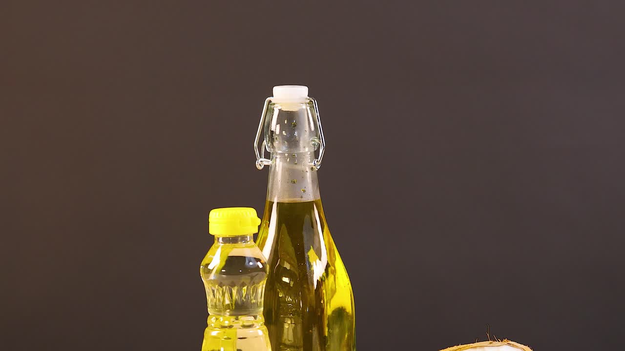 A variety of oils and foods including avocados, coconuts, and almonds arranged on a table with warm lighting