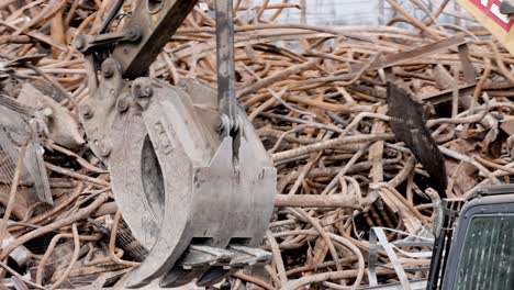 excavator demolishing building moving large pieces of metal with a mountain of metal behind it