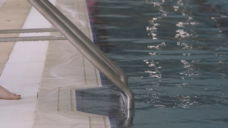 Primo piano dei piedi di una giovane donna che entrano nella scaletta in una piscina coperta.