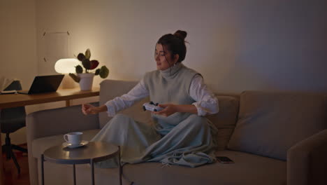 smiling gamer holding joystick playing video game at home. woman drinking tea