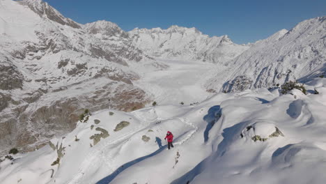 aerial shot in switzerland with a person walking with snow shoes on a sunny day with a glacier behind