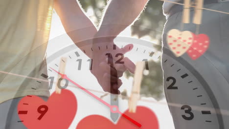 animation of moving clock and hearts over caucasian couple holding hands