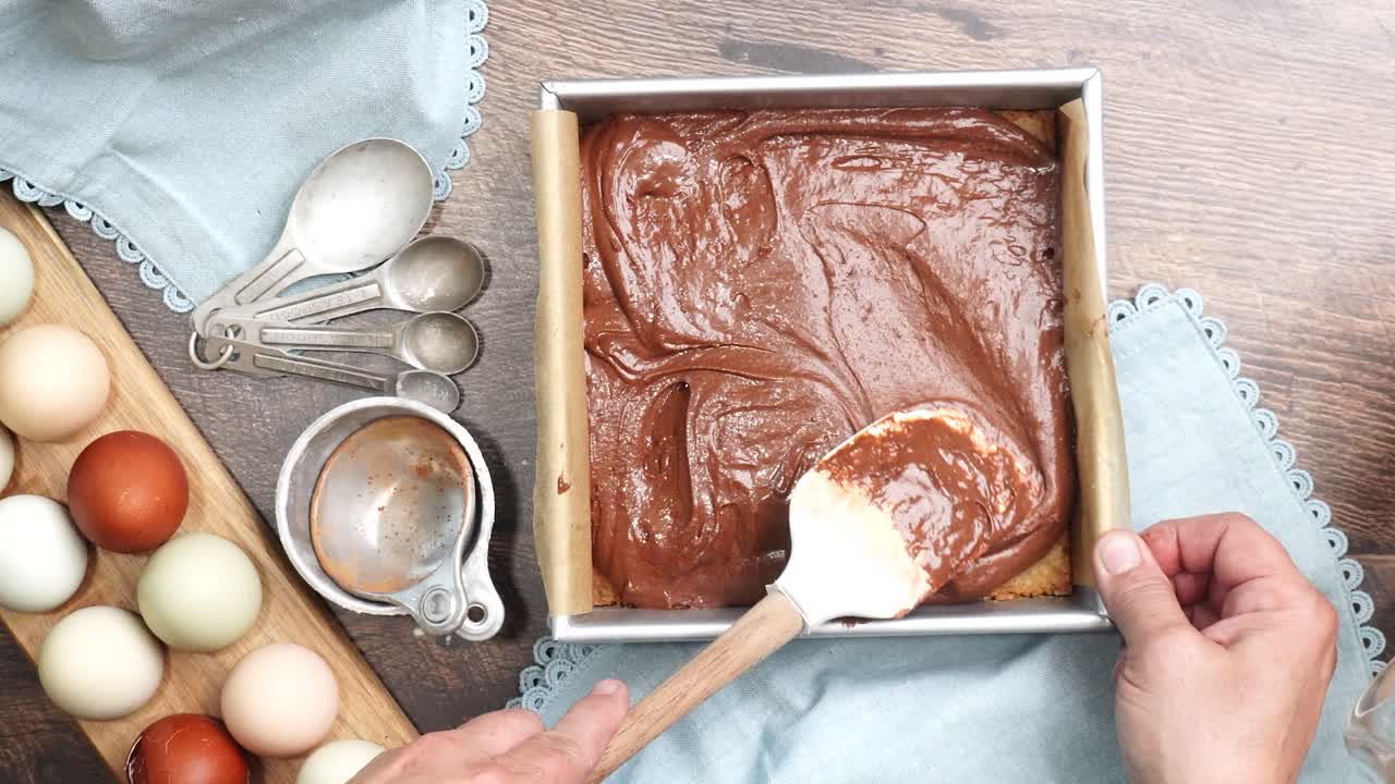Baking delicious caramel pecan brownies. Spreading the brownie batter over the crust in a square baking pan. Freshly baked gooey chocolate brownies with sweet caramel and nutty pecans.