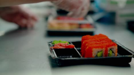 el cocinero sirve rollos japoneses con caviar de pescado volador cierra los paquetes para su posterior entrega al cliente