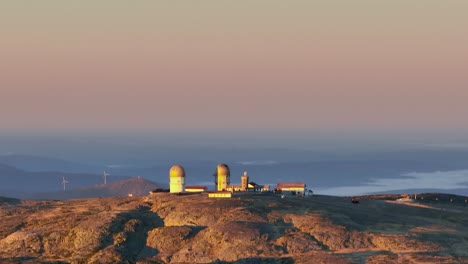 Sunrise-aerial-riser-view-reveals-abandoned-radar-towers-of-observatory,-Covilha