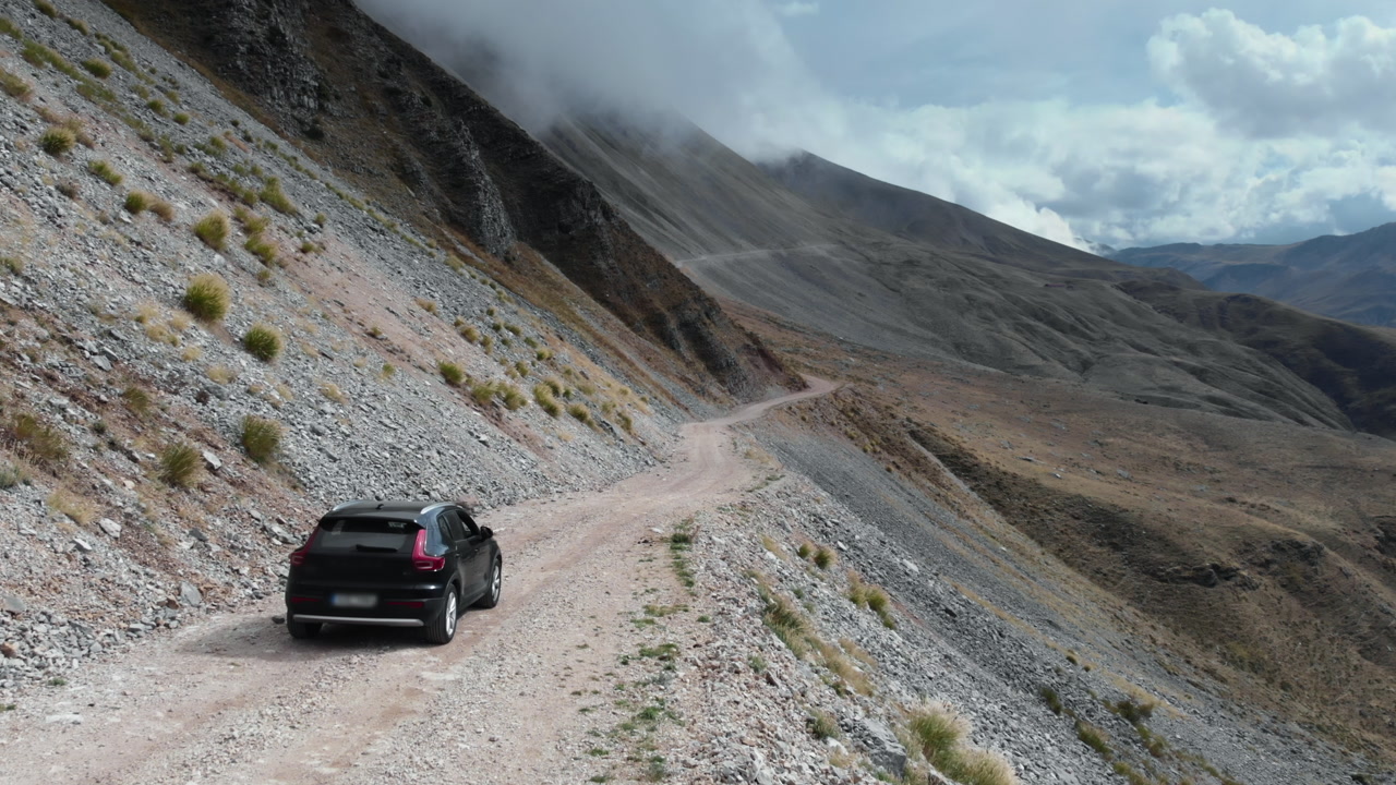 An SUV makes its way along a steep, rocky mountain trail under a blanket of clouds. Ideal for themes of adventure and exploration in rugged landscapes.