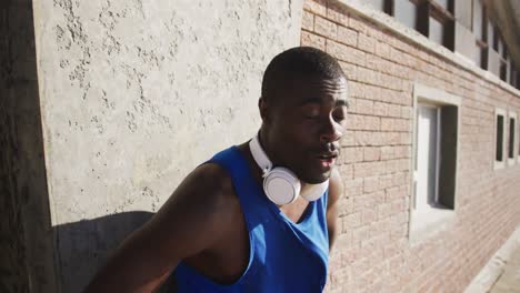 Hombre-Afroamericano-Sonriente-Con-Auriculares-Tomando-Un-Descanso-En-El-Ejercicio-Al-Aire-Libre