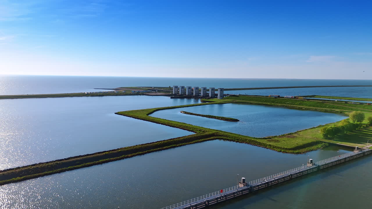 Flying closer to the dikes on the lake in Lelystad, the Netherlands. Approaching the dam with sluices. Aerial view.