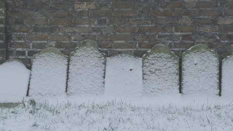 anonymous snow covered headstones against red brick wall on a winter day in a graveyard