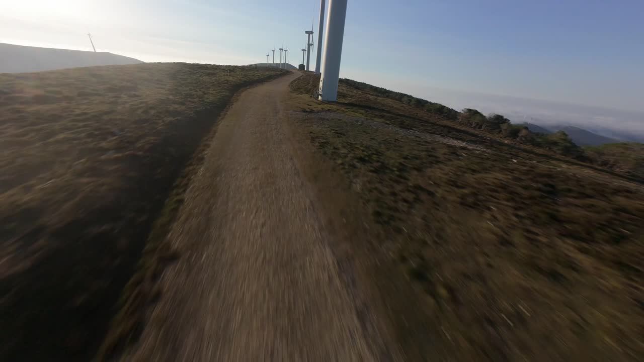 Volo FPV ad alta velocità lungo la strada di accesso alle turbine eoliche, sfrecciando attraverso le strette curve di montagna e trasmettendo una sensazione di potenza, vertigine e movimento dinamico