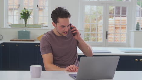 transgender man using mobile phone working from home using laptop on kitchen counter