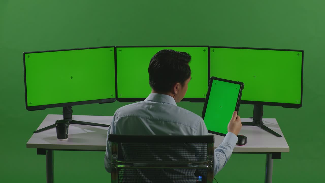 hombre de negocios trabajando en un escritorio con múltiples monitores de pantalla verde y tableta
