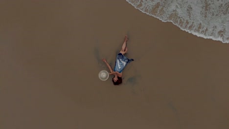 4k aerial top down drone shot of a pretty 27-year-old young indian woman getting drenched by the sea waves along the shores of varkala