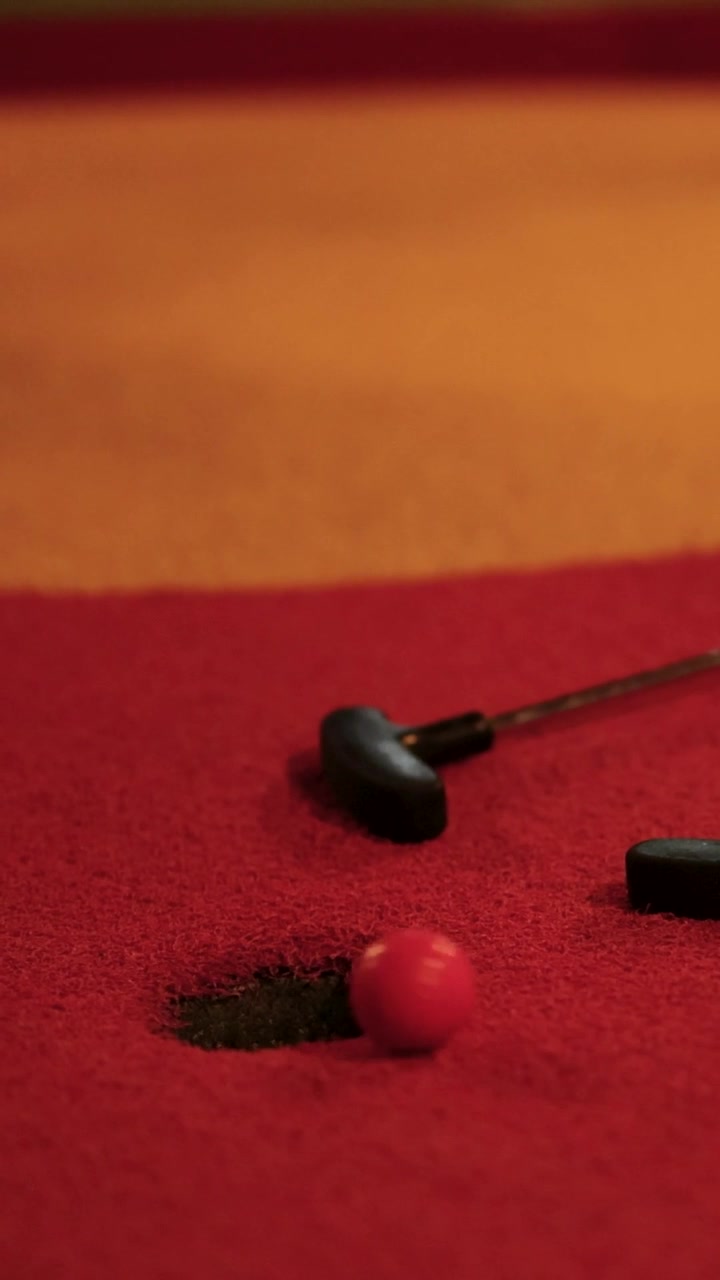 Pallina da minigolf rossa che rotola nella buca