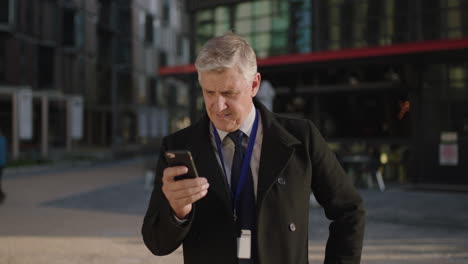 portrait of successful businessman checking messages using smartphone looking at camera smiling confident in city