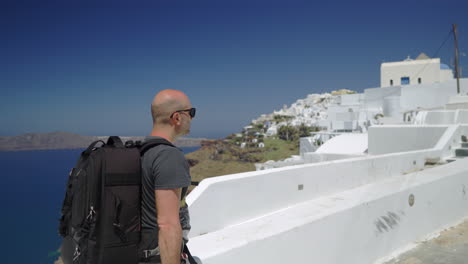 following from the side a man walking in santorini, greece, wearing a backpack