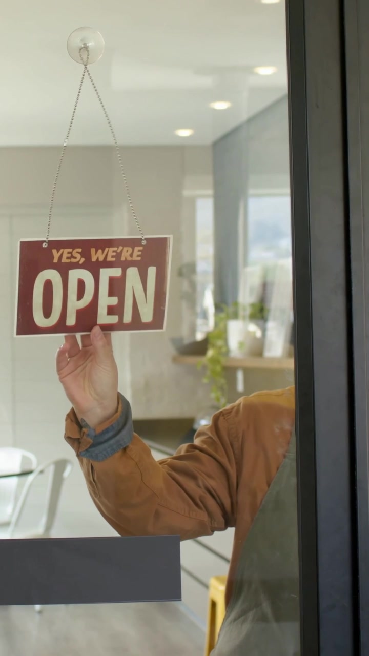 Vertical video: Turning owner in apron flipping closed sign at door, welcoming guests, copy space