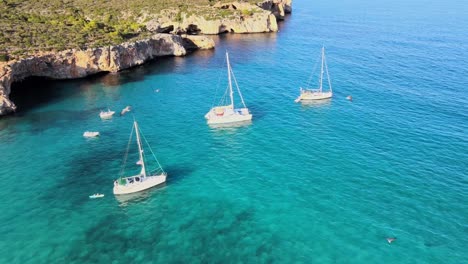 clear turquoise waters surround sailboats anchored near the stunning cliffs of cala varques. this serene location in majorca offers breathtaking views and tranquil vibes perfect for relaxation.