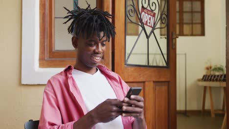 Happy-african-american-craftsman-using-smartphone-in-leather-workshop